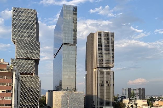 Torres de usos mixtos en Guadalajara, Jalisco, rodeadas de edificios de menor altura y arbolado urbano bajo un cielo despejado.
